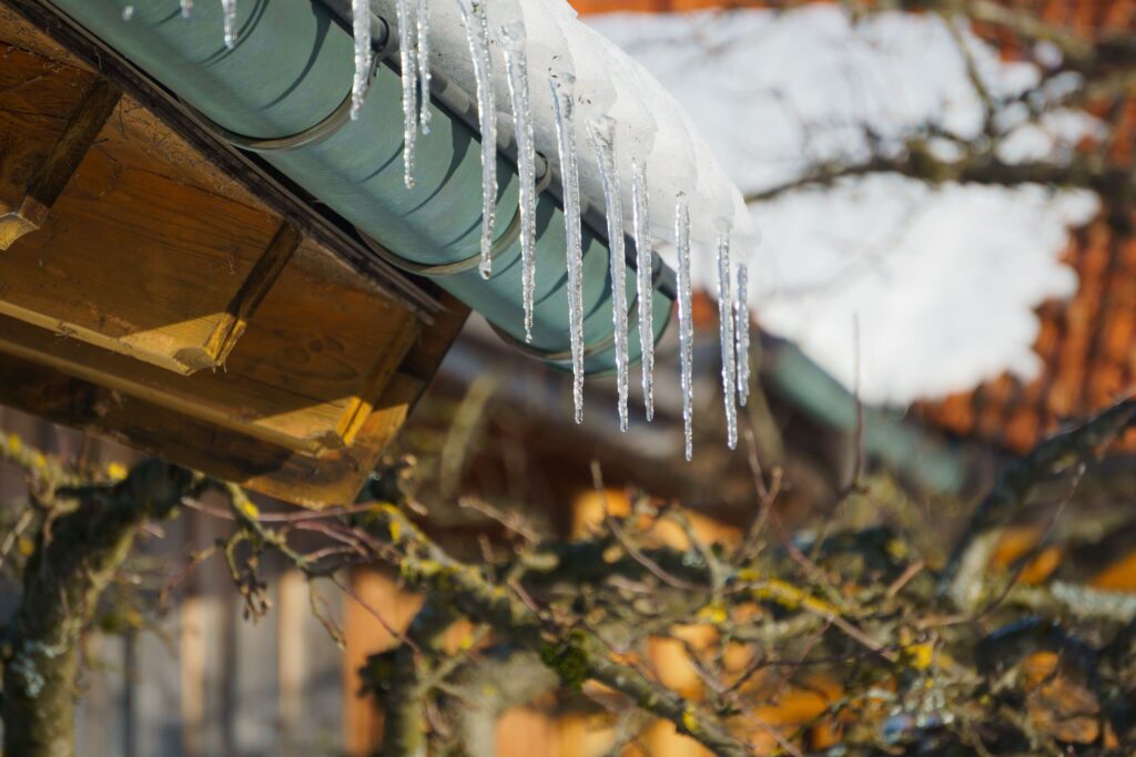 Closeup of ice dams hanging from a roof with sunlit blurred background