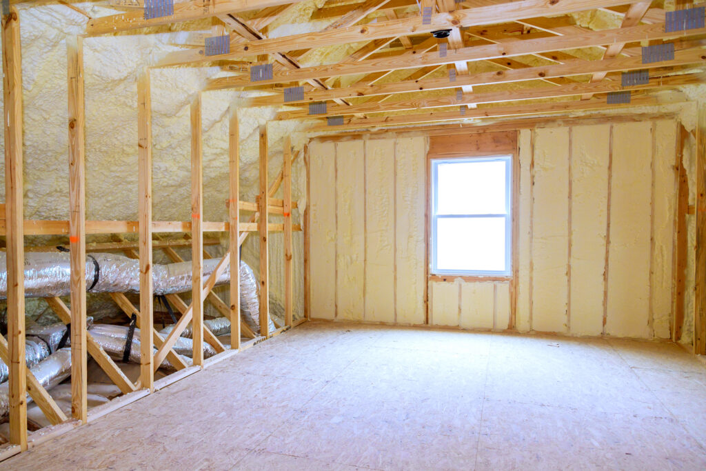 Spray foam insulation installed on attic roof decking and wall cavities with exposed framing and HVAC ductwork in an unfinished attic.