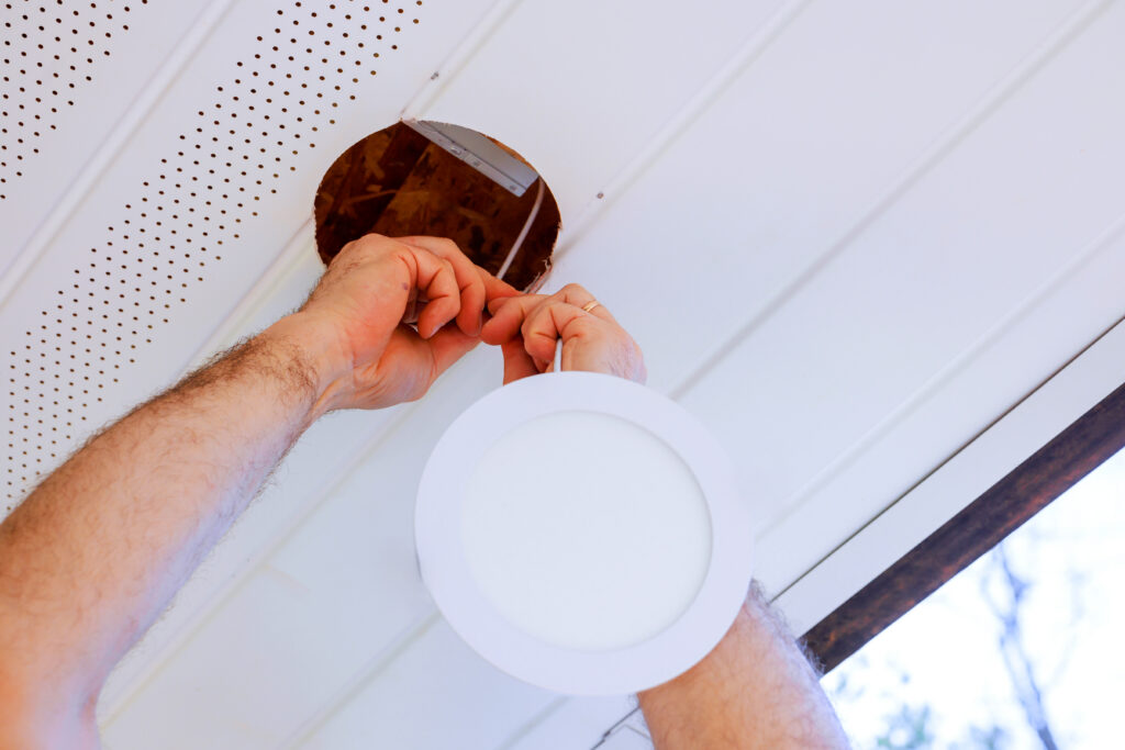 Electrician installing a recessed LED light fixture in a white ceiling.